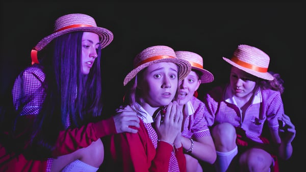 Un grupo de alumnas del Cheltenham Ladies' College lleva ropa colorida y sombreros en un entorno oscuro.