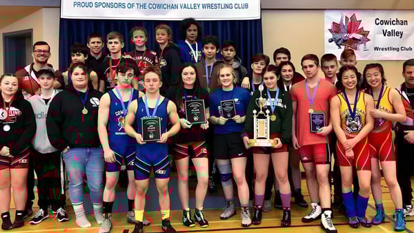 Un grupo de jóvenes luchadoras de la Chemainus Secondary School está con trofeos frente a una pancarta del Cowichan Valley Wrestling Club.
