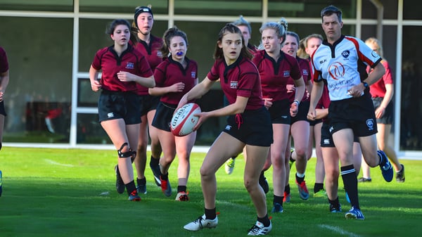 Un grupo de jugadoras de rugby de la Chemainus Secondary School está en un campo de césped con un equipo contrario al fondo.