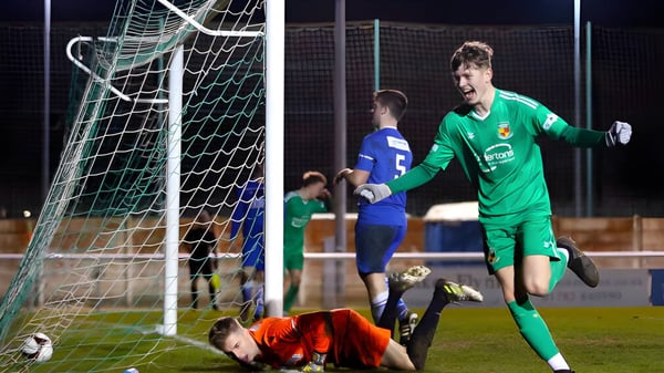 Un portero con camiseta verde realiza una parada durante el partido de fútbol en el campo de Cheshire College South & West.