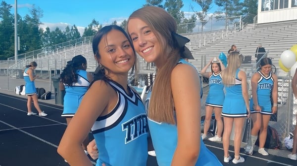 Dos estudiantes en uniformes de animadoras se abrazan en el campo deportivo del Chesterfield School District.