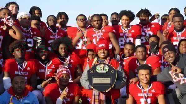 Un grupo de estudiantes de Chicago Public Schools lleva camisetas rojas y sostiene un trofeo en una premiación al aire libre.
