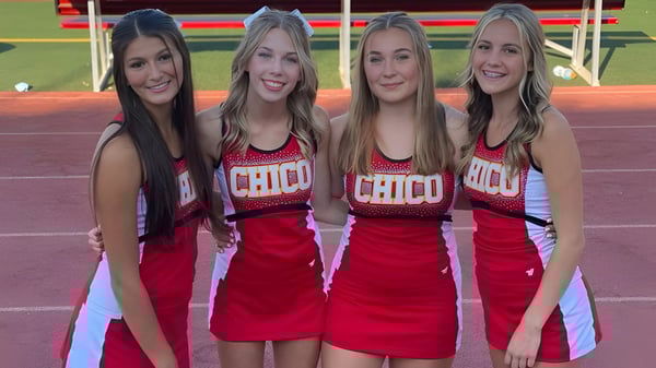 Cuatro estudiantes en uniformes rojos de animadoras están en el campo de deportes del Chico Unified School District.