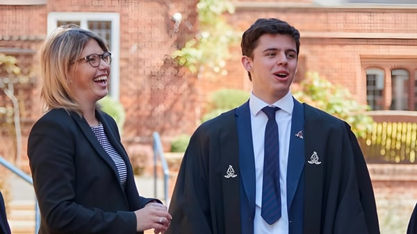 Dos estudiantes están de pie frente a un edificio de ladrillo en el campus de la Chigwell School y mantienen una conversación.