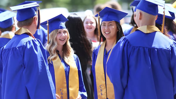 Un grupo de graduados de la Chilliwack Secondary School está con togas y birretes azules juntos frente a un fondo verde.
