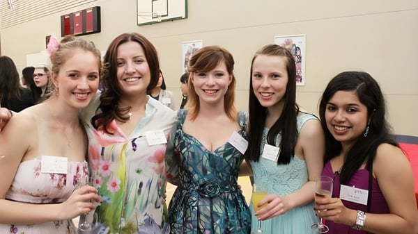 Un grupo de jóvenes alumnas de la Chilton Saint James School posan con vestidos coloridos frente a una canasta de baloncesto.