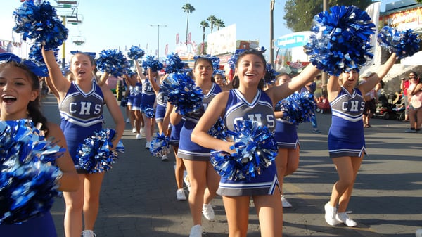 Porristas en uniformes azules y blancos marchan con pompones a lo largo de una calle flanqueada por palmeras en el Chino Valley Unified School District.