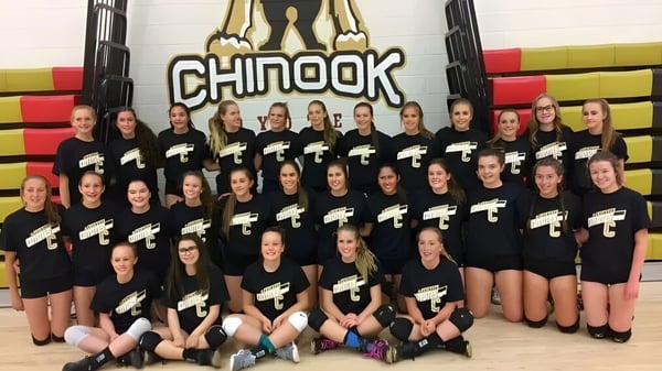 Un grupo de jóvenes atletas de la Chinook High School posan en el gimnasio frente a colchonetas y equipos.