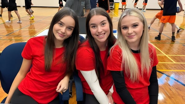 Tres alumnas de la Chippewa Secondary School en camisetas rojas posan en un gimnasio.