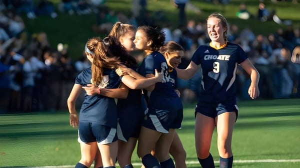 Un grupo de jóvenes futbolistas de Choate Rosemary Hall celebra juntos en un campo de hierba frente a espectadores.