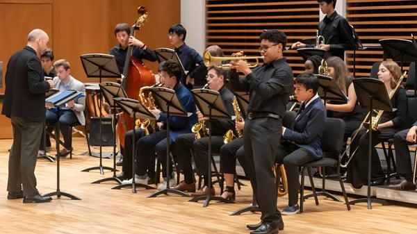 Una orquesta de Choate Rosemary Hall toca bajo la dirección de un director en el escenario frente al público.