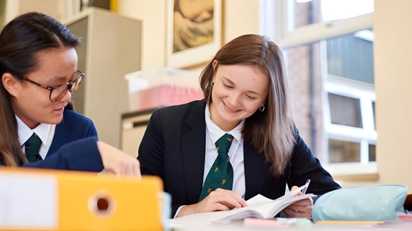 Dos alumnos en uniformes escolares trabajan juntos en una tarea en la mesa en Christ College.