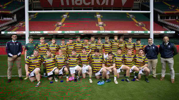 Un grupo de alumnas y alumnos en camisetas a rayas posan en el campo deportivo de Christ College frente a un gran estadio.