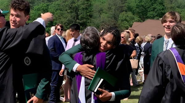 Un grupo de graduados en togas se reúne al aire libre en el campus de la Christ School.