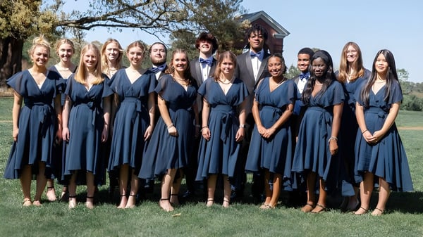 Estudiantes de la Christchurch School están al aire libre en un prado y actúan como coro.