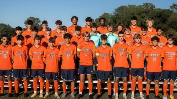 Un grupo de jóvenes futbolistas de la Christchurch School está de pie juntos en un campo con árboles y cielo azul.