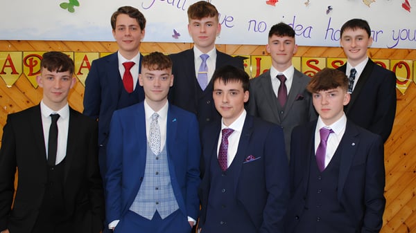 Un grupo de estudiantes de la Christian Brothers School Kilkenny está vestido con ropa formal frente a un colorido fondo de aula.