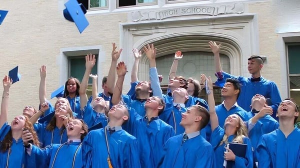 Estudiantes de la Christian Central Academy celebran su graduación en túnicas azules frente al edificio escolar.