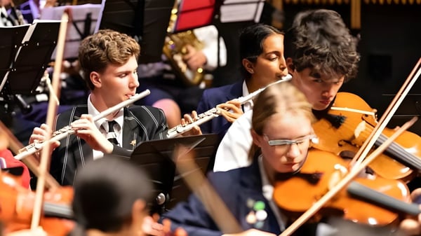 Un grupo de estudiantes del Christ's College toca diferentes instrumentos en un escenario con un fondo colorido.