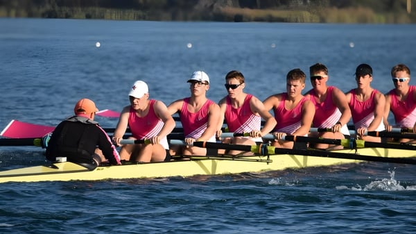 Un grupo de estudiantes de la Christ's Hospital School rema en uniformes rojos en un bote amarillo en un lago tranquilo.