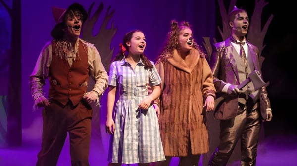 Un grupo de cuatro disfrazados realiza una actuación en el escenario de Cincinnati Christian Schools frente a un fondo violeta.