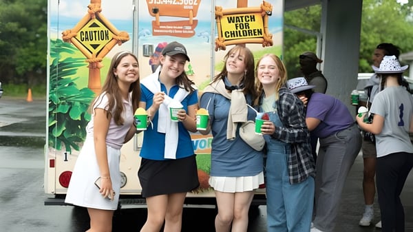 Un grupo de estudiantes de Cincinnati Christian Schools está frente a un colorido fondo de carnaval con carteles y decoraciones.