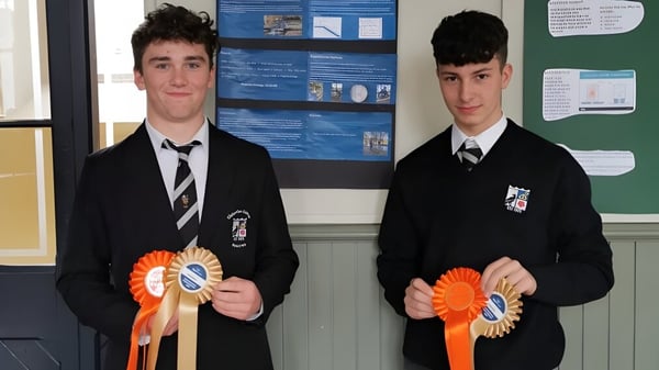 Dos estudiantes en uniformes escolares sostienen cintas naranjas frente a un tablón de anuncios en el campus del Cistercian College.