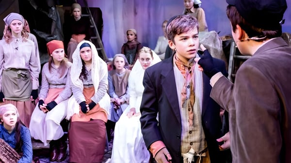 Un grupo de estudiantes de la Claremont School está en un escenario en un espacio de actuación frente a cortinas y luces.