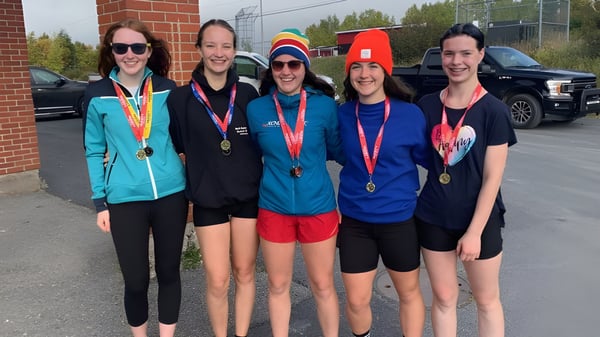 Un grupo de cinco deportistas con medallas está frente a un edificio de ladrillo en el terreno de la Clarenville High School.