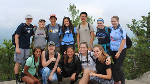 Un grupo de estudiantes del Clarin College posan juntos al aire libre frente a árboles y un cielo nublado.