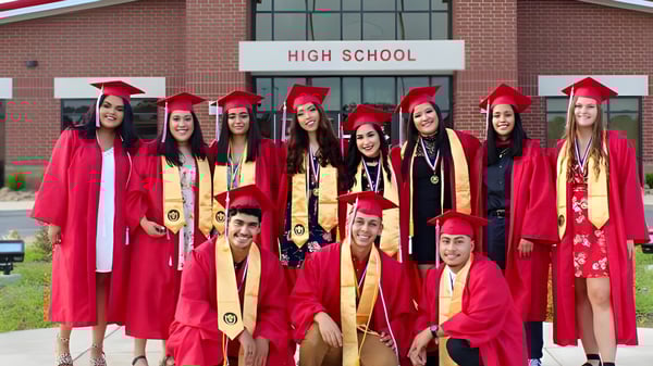 Un grupo de graduadas y graduados de la Clarksville High School están en togas rojas frente al edificio escolar celebrando su graduación.
