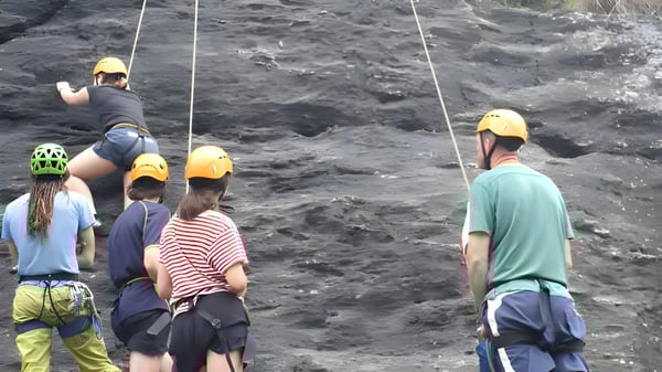Estudiantes del Classic Plus Programm llevan cascos de protección y están con arneses en un terreno rocoso durante una actividad al aire libre.