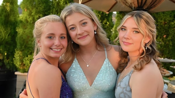 Tres estudiantes de la Clayton Heights Secondary School posan juntas al aire libre frente a un fondo de árboles verdes.