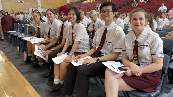 Un grupo de alumnas de la Cleveland District State High School está sentada en filas mirando hacia un escenario y asientos para espectadores en el fondo.