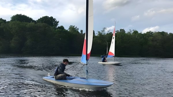 Una persona navega en un pequeño bote sobre el agua con el fondo de árboles en el terreno del Clifton College.