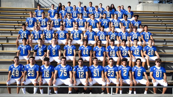 Un gran grupo de estudiantes en uniformes azules está en las gradas del estadio del Clovis Unified School District.