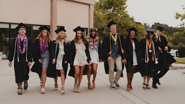 Un grupo de graduados está en túnicas de colores frente a un edificio en el campus de la Coastal Christian School.