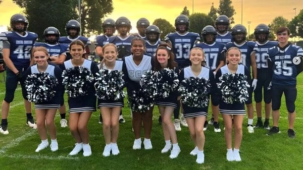 Estudiantes de la Coastal Christian School posan juntos como futbolistas y animadoras en un campo de césped al atardecer.