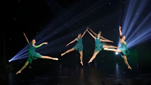 Un grupo de bailarinas y bailarines de la Cobham Hall School realizan una acrobacia aérea sincronizada en un escenario oscuro.