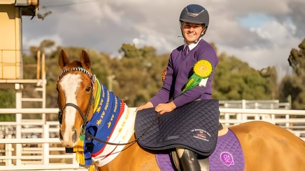 Una persona en uniforme morado monta un caballo decorado de colores en el terreno del Coffs Harbour Senior College.
