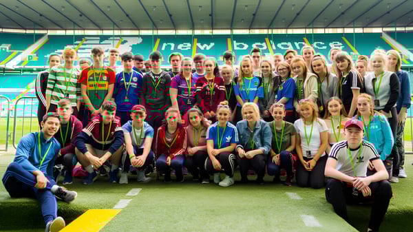 Un grupo de estudiantes está en el campo de deportes de la Coláiste an Chreagáin con camisetas deportivas y ropa de ocio.