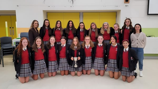 Un grupo de alumnas en uniformes rojos y negros está juntas en el campus de la Coláiste Bhaile Chláir.