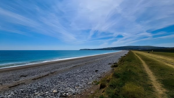 Un paisaje costero con playa de guijarros y camino cubierto de hierba cerca de Coláiste Chill Mhantáin.