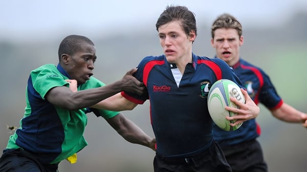 Dos jugadores de rugby de Coláiste Chill Mhantáin realizan un tackle en el campo de césped.