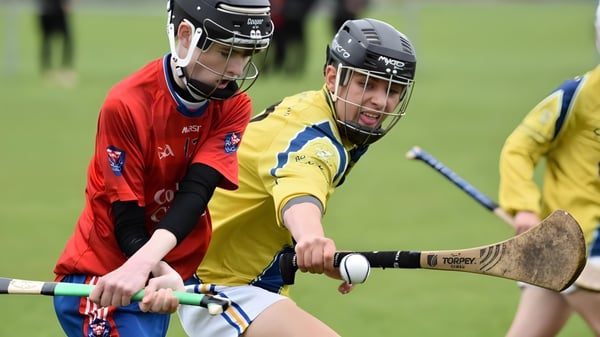 Dos jóvenes atletas en uniformes deportivos participan en una competencia en el campo de deportes de la Coláiste Choilm.