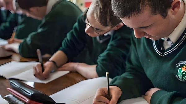Estudiantes en uniformes escolares están concentrados en sus mesas durante la clase de Coláiste Chríost Rí.