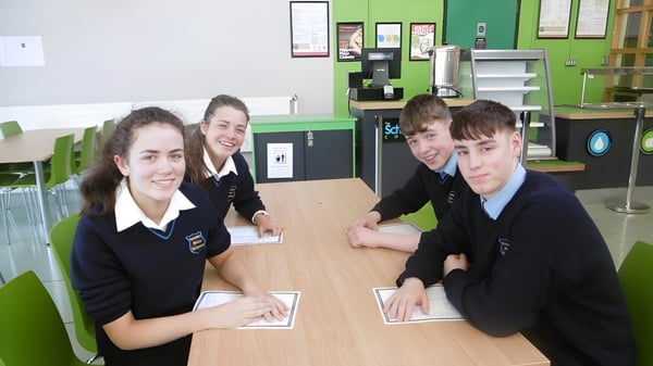 Alumnos de Coláiste Mhuire Ballymote están sentados en uniformes escolares en una mesa en el aula.