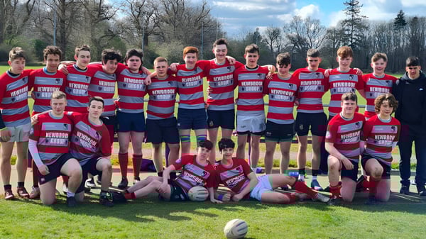 Un grupo de jóvenes deportistas en camisetas rojas y azules está de pie en el campo deportivo de la Coláiste Mhuire Mullingar.