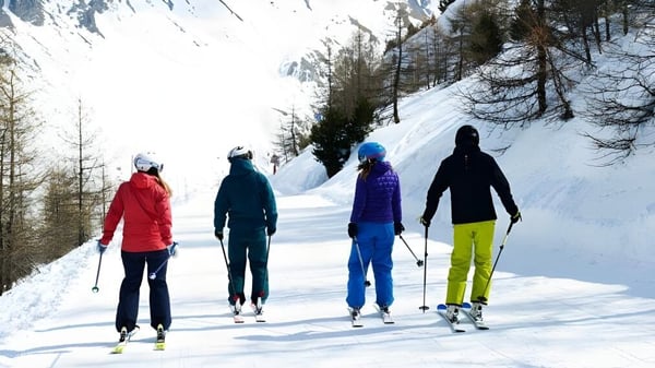 Estudiantes de Coláiste Muire Crosshaven esquiando por un camino nevado con árboles de pino y montañas.