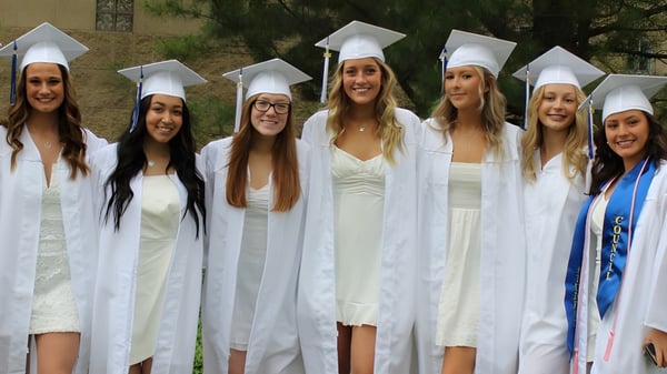 Un grupo de jóvenes mujeres en togas de graduación blancas está reunido en el terreno de Coláiste Muire Crosshaven.